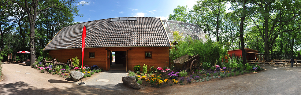 A panoramic view of a rural visitor centre with flowerbeds and trees.